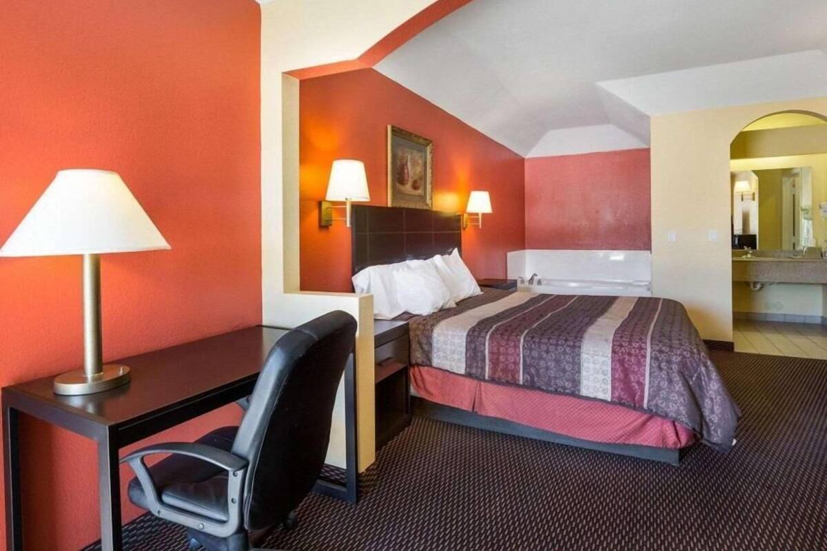 A hotel room with a bed, desk, chair, and a bathroom visible through an archway.