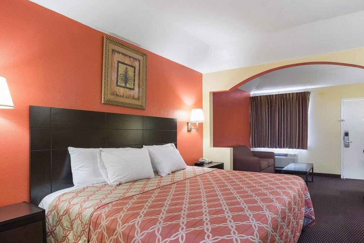 A hotel room with a large bed, a nightstand, a desk, a chair, and a door.