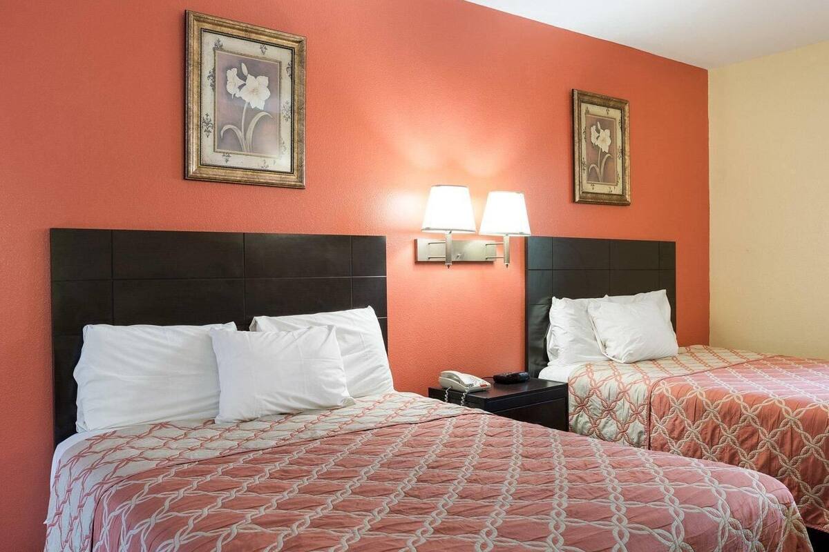A hotel room with two beds, a nightstand with a phone and lamp, and two wall-mounted lamps.