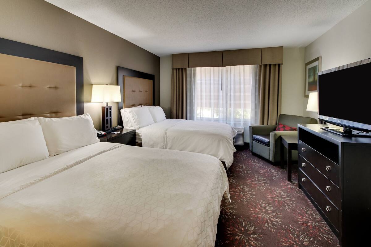 A hotel room with two beds, a TV, a desk, and a dresser.