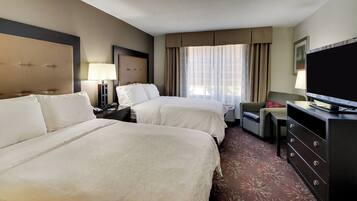 A hotel room with two beds, a desk, a television, and a dresser.