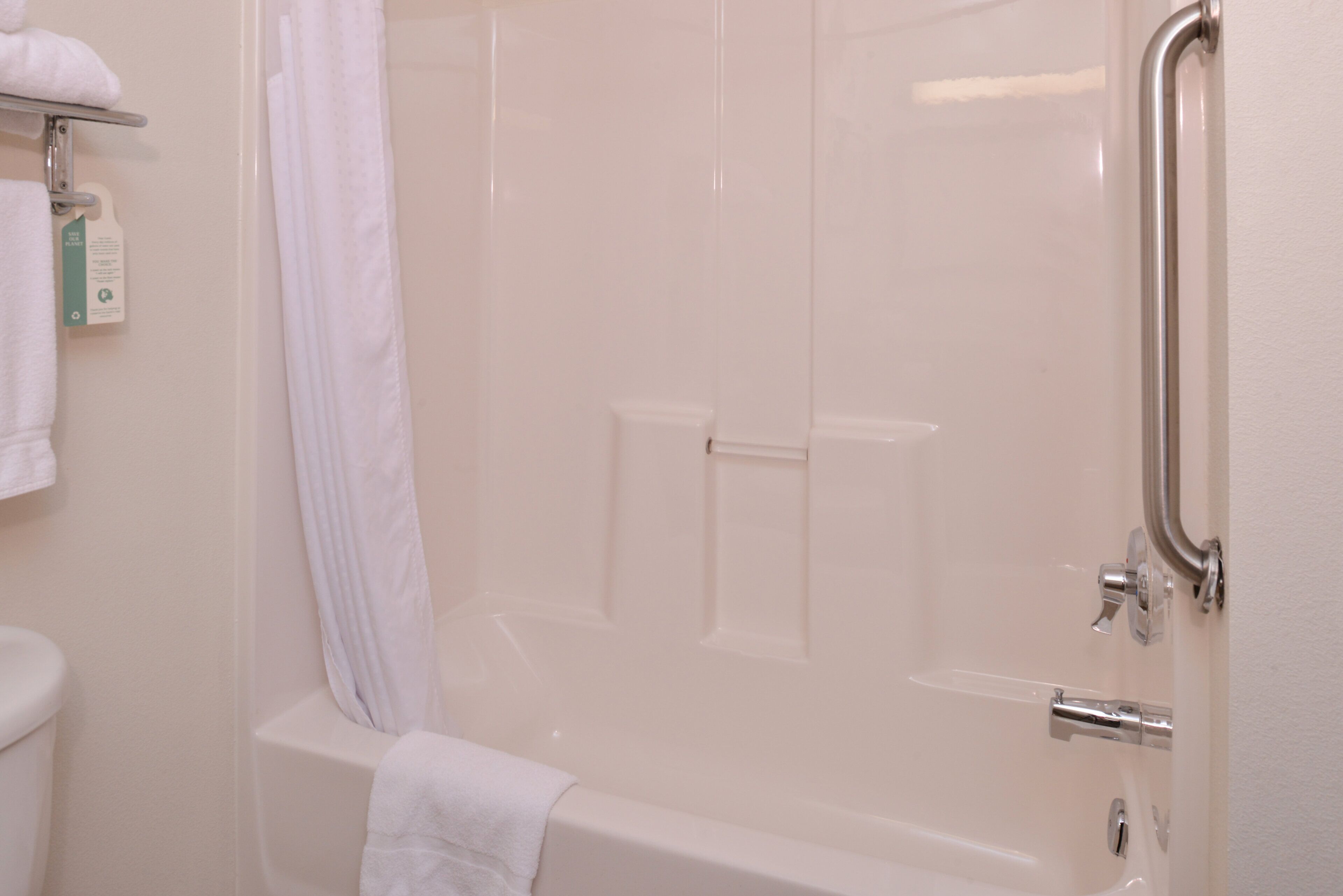 A bathroom with a bathtub, a shower curtain, and a handrail.