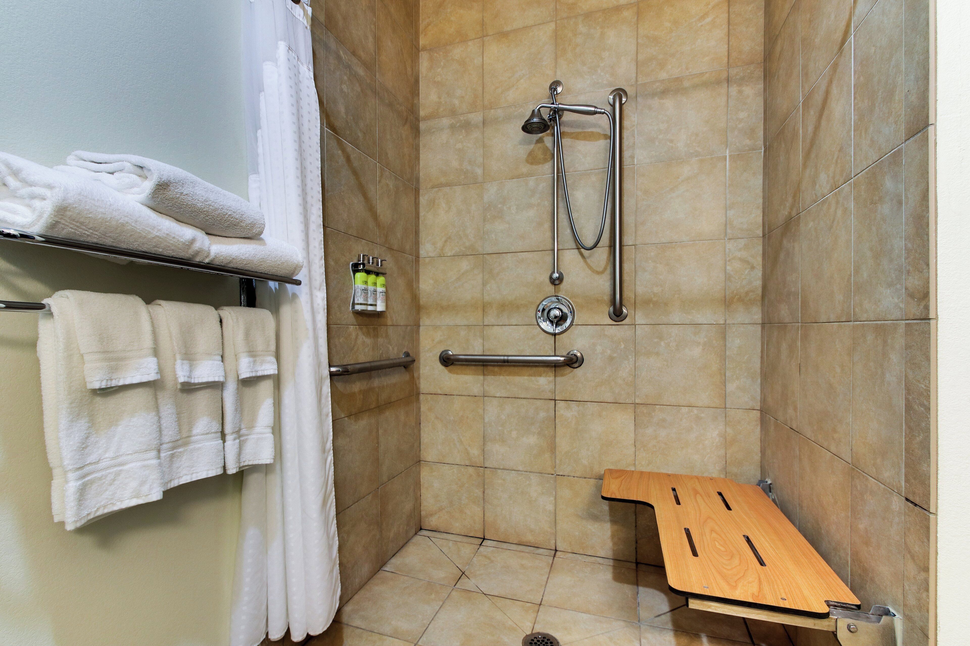 A shower area with a handheld showerhead, a handheld shower attachment, and a wooden bench.