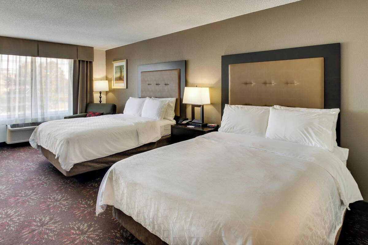 A hotel room with two beds, a desk, a chair, and a window with curtains.