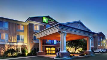 Un hotel Holiday Inn Express & Suites con entrada cubierta, fachada de ladrillo y un estacionamiento bien iluminado.