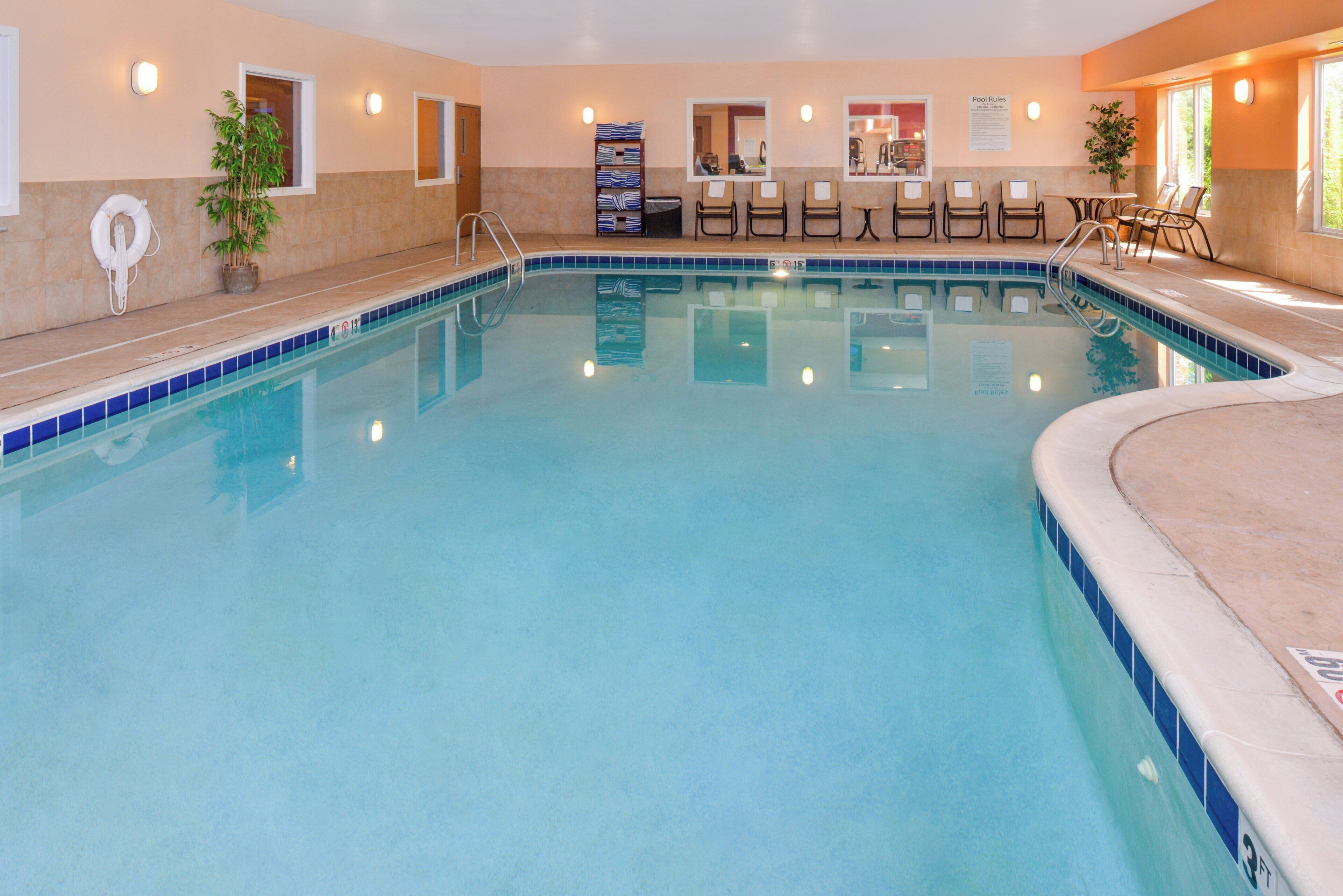 Una piscina interior con agua cristalina, una silla de salvavidas y un área de descanso junto a la piscina.