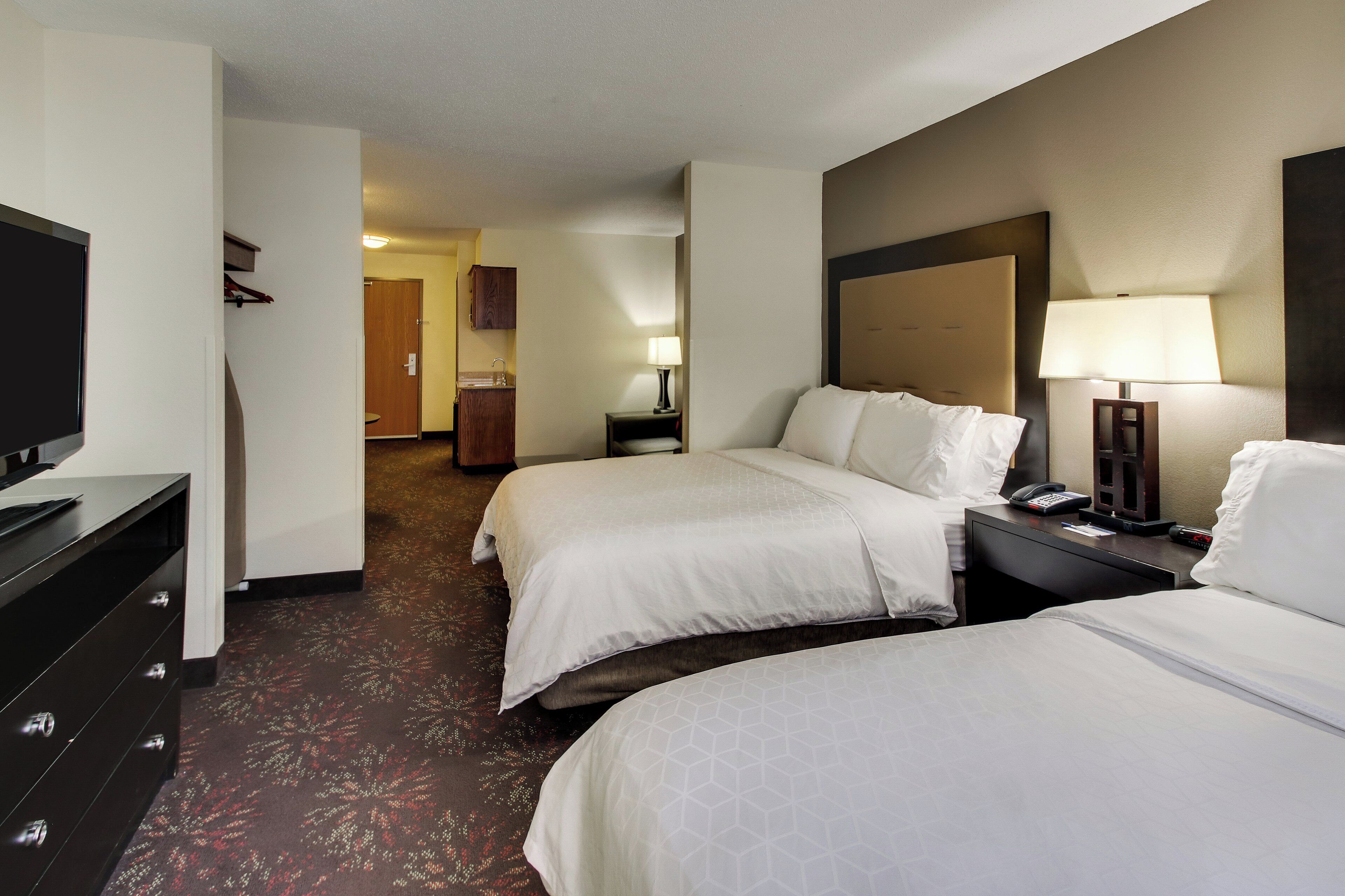 A hotel room with two beds, a television, a desk with a lamp, and a bathroom visible in the background.