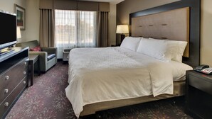A hotel room with a large bed, a desk with a television, a chair, and a nightstand with a phone.