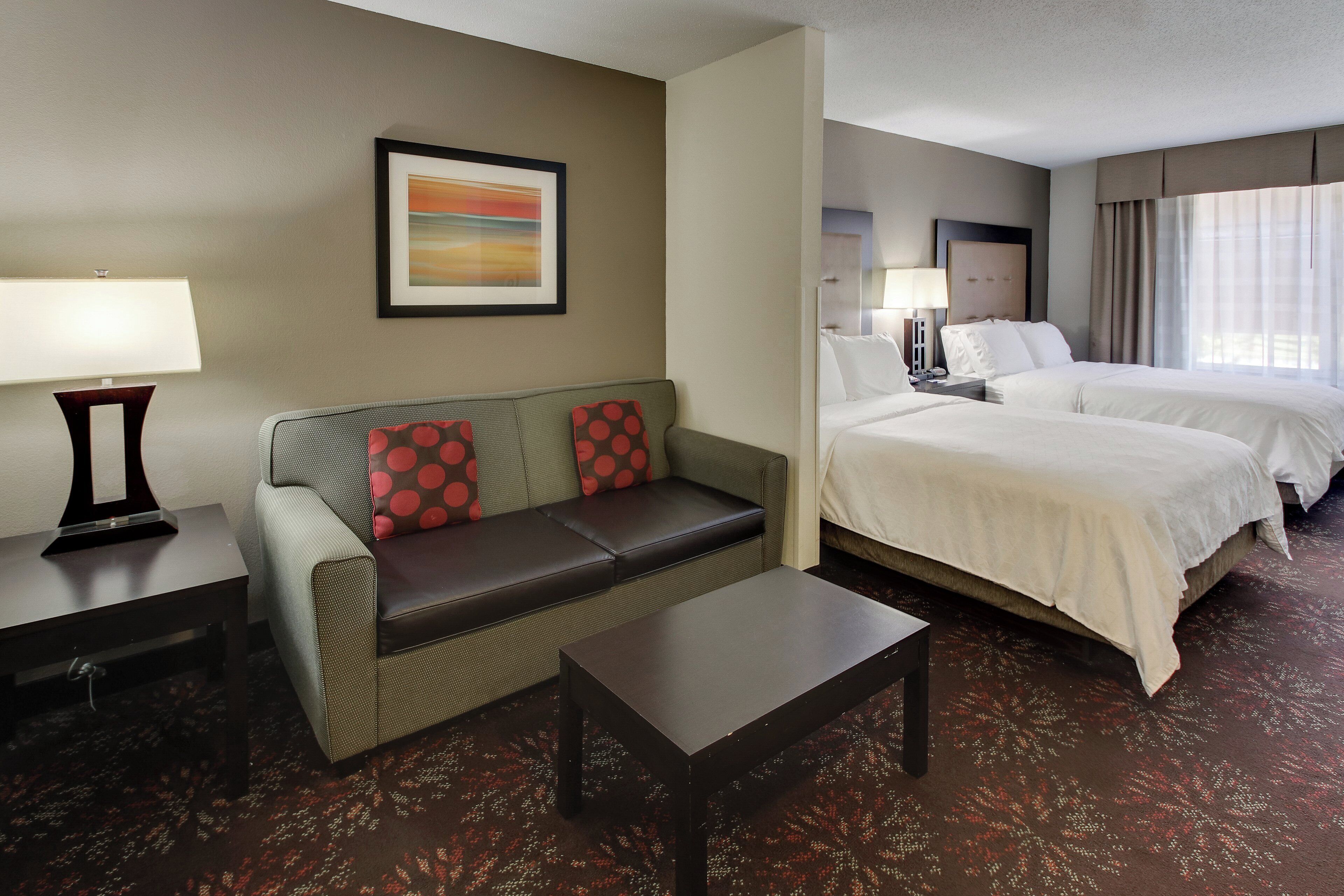 A hotel room with a sofa, a bed, a desk, and a framed picture on the wall.
