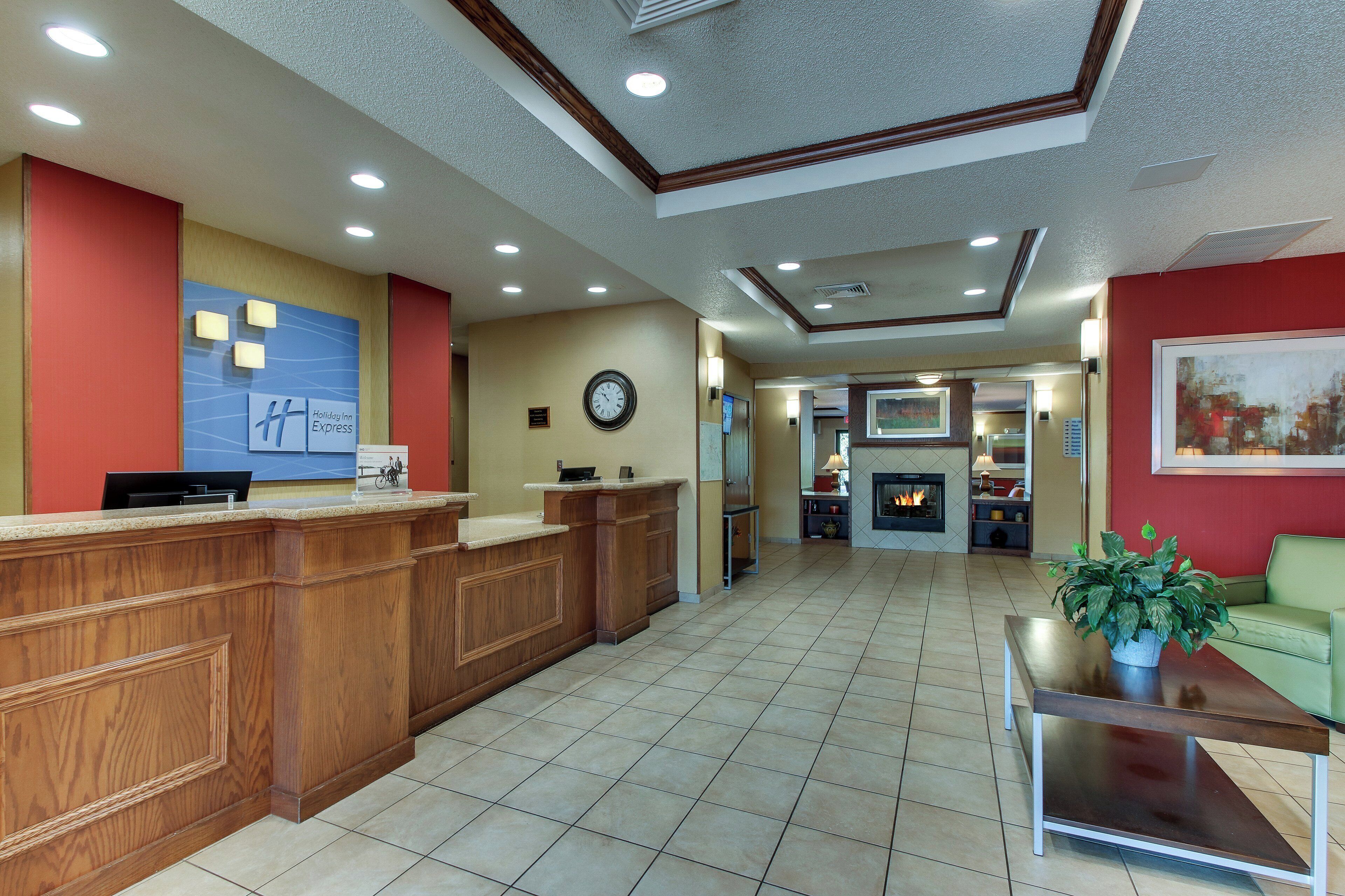 A hotel lobby with a reception desk, a clock, a fireplace, and a green sofa.