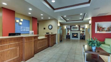 A hotel lobby with a reception desk, a clock, a fireplace, and a green sofa.