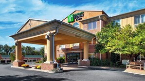 A Holiday Inn Express & Suites building with a covered entrance, brick facade, and landscaped area with plants.