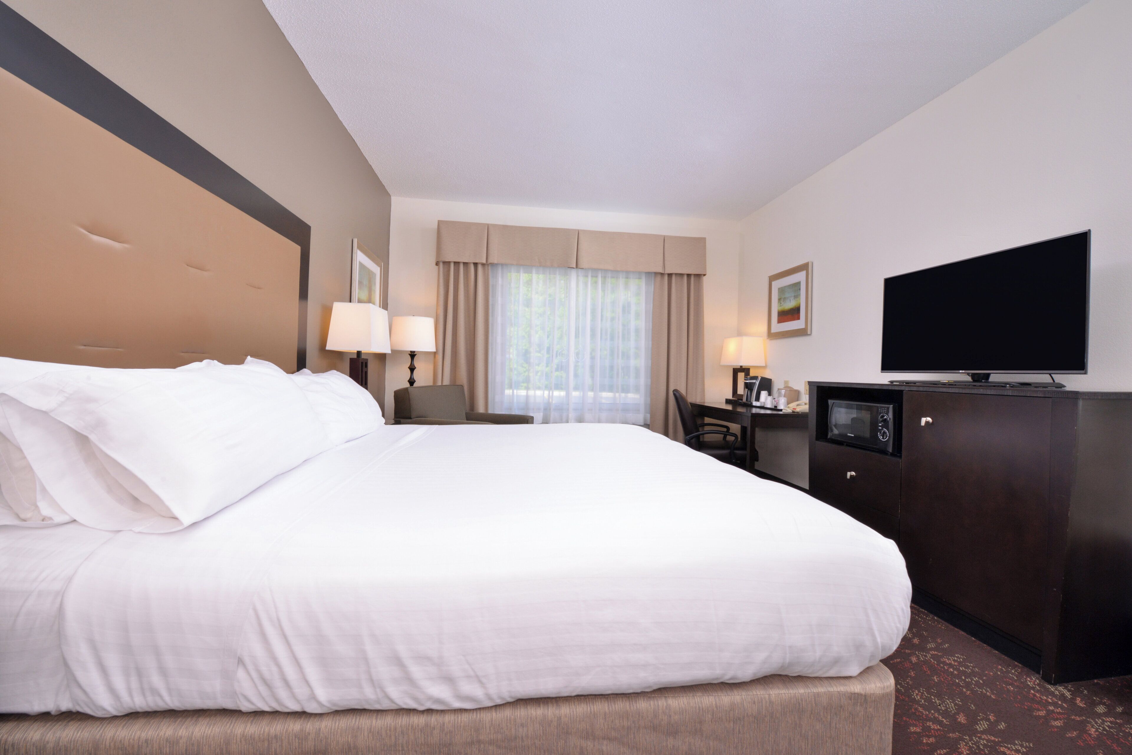 A hotel room with a large bed, a desk, a chair, a television, and a window with curtains.