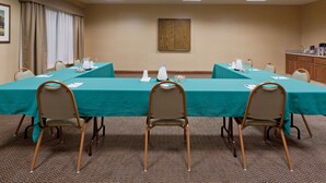 A conference room with a long table, four chairs, a wooden cabinet, and a painting on the wall.