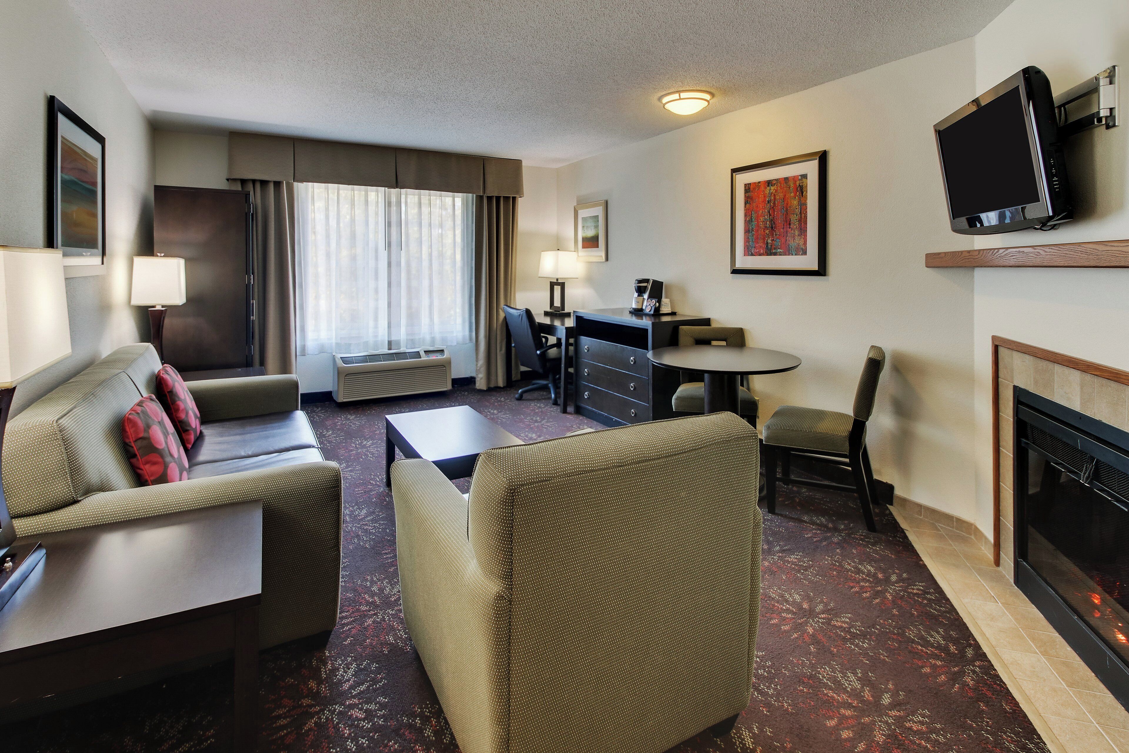 Een hotelkamer met een bank, fauteuil, salontafel, flatscreen-televisie, open haard en een bureau met lamp.