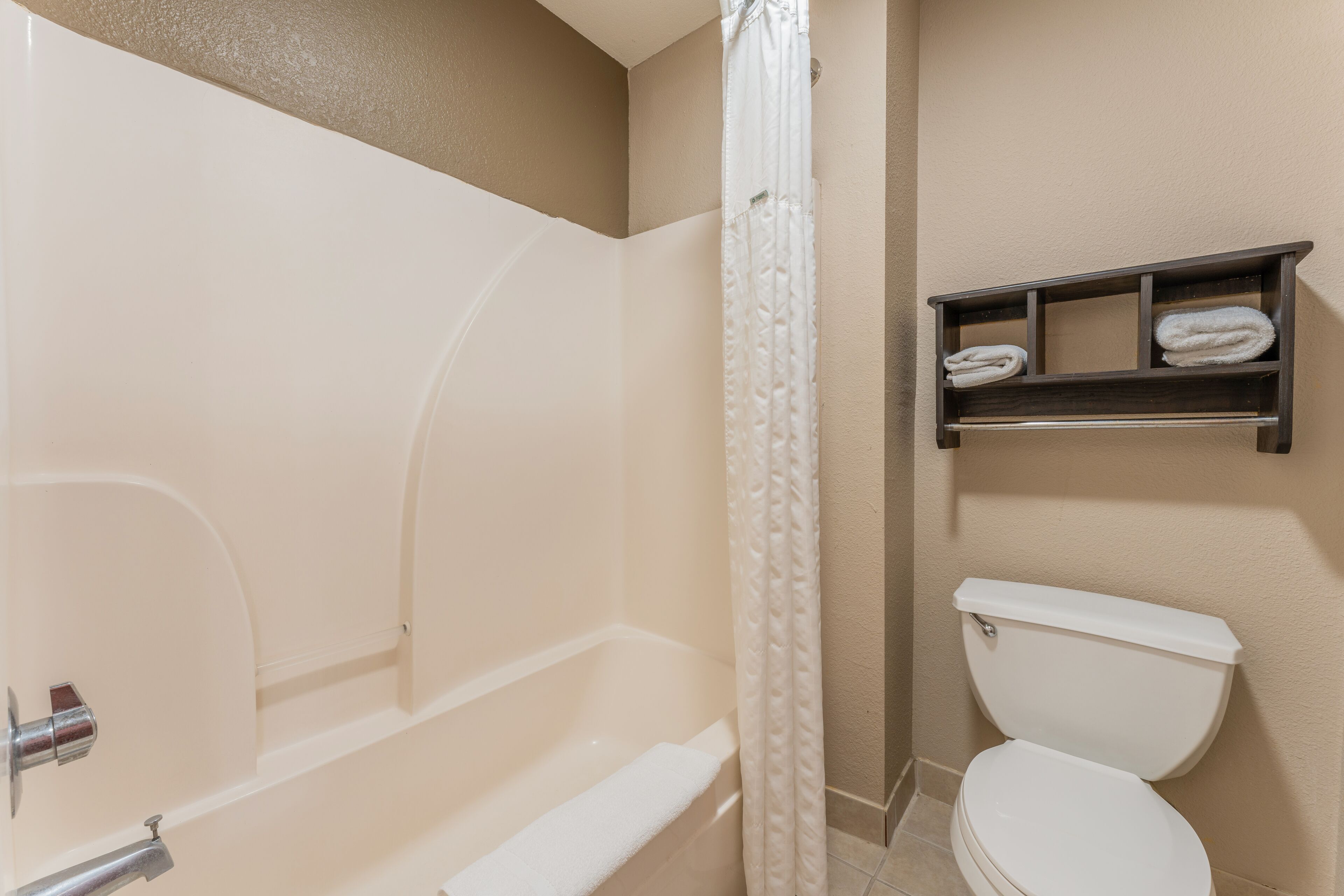 A bathroom with a bathtub, toilet, and a shelf with towels.