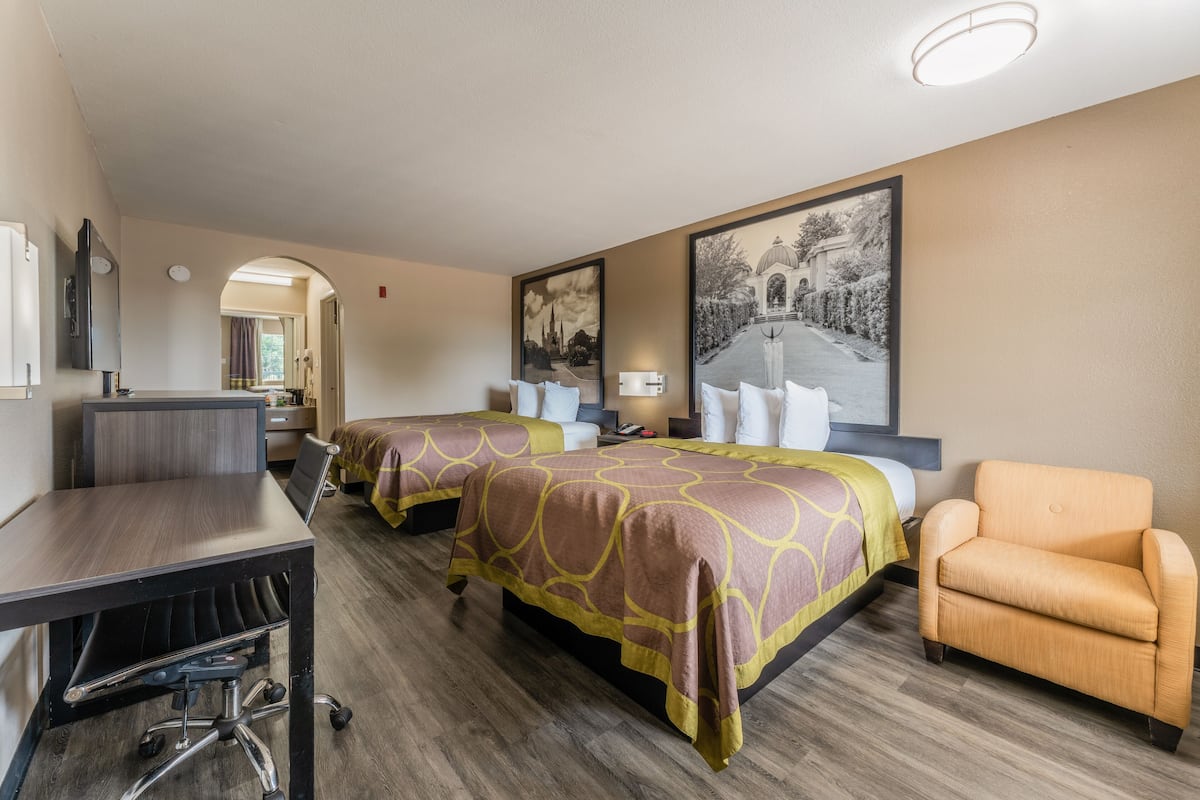 A hotel room with two beds, a desk, and a chair.
