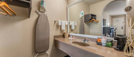 A bathroom with a sink, mirror, and hanging clothes rack.