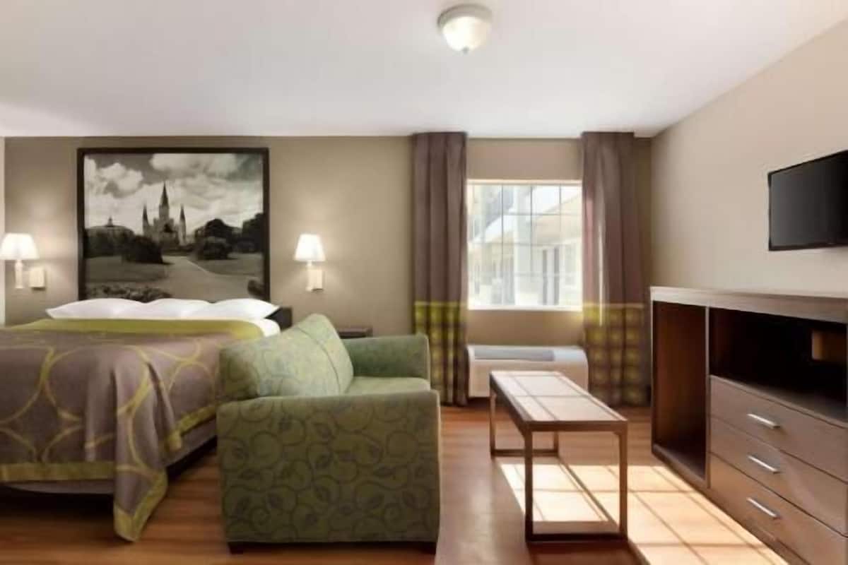A hotel room with a bed, a sofa, a TV, a desk, and a window with curtains.