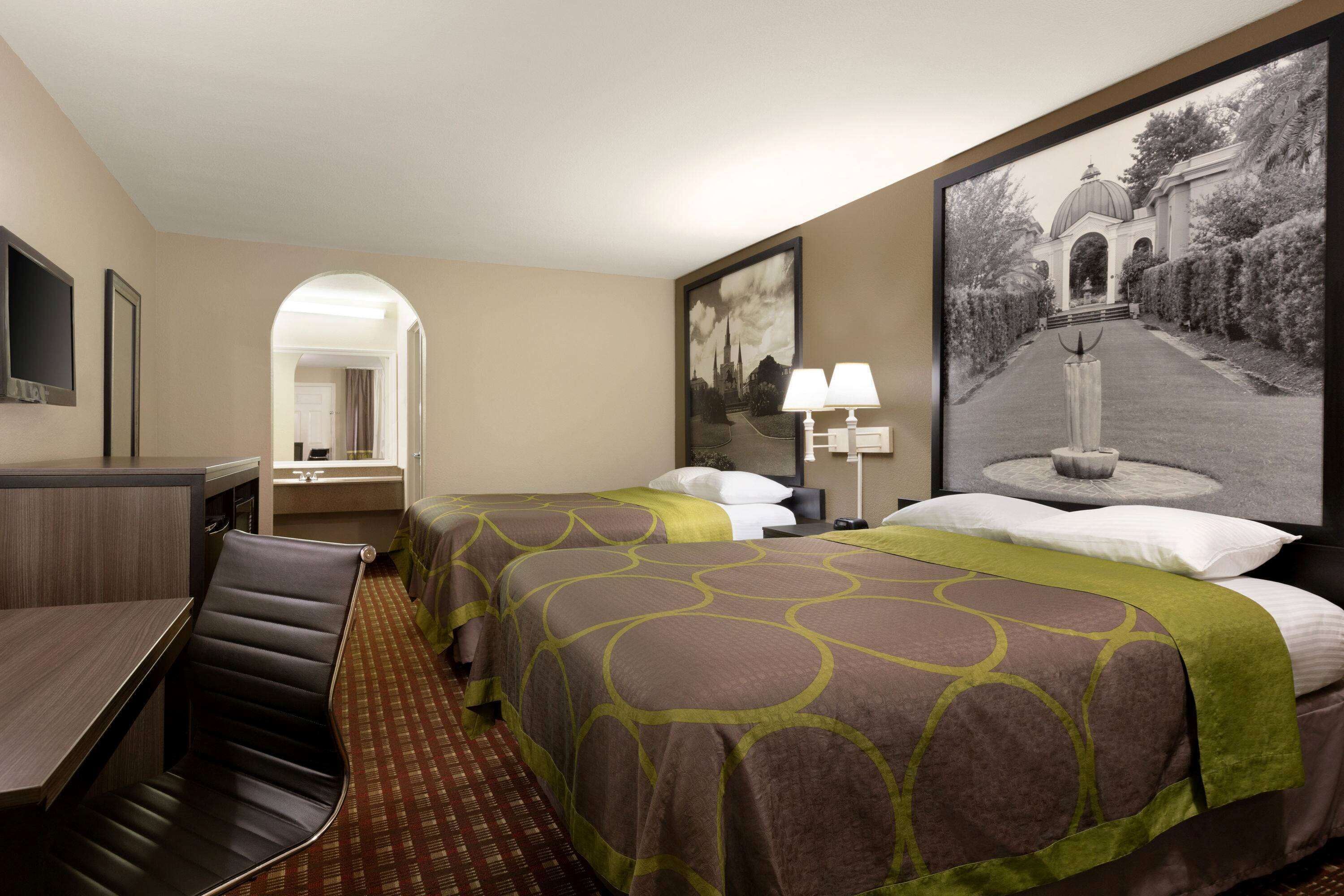 Habitación de hotel con dos camas, un escritorio, una silla, un espejo y un cuadro en la pared.