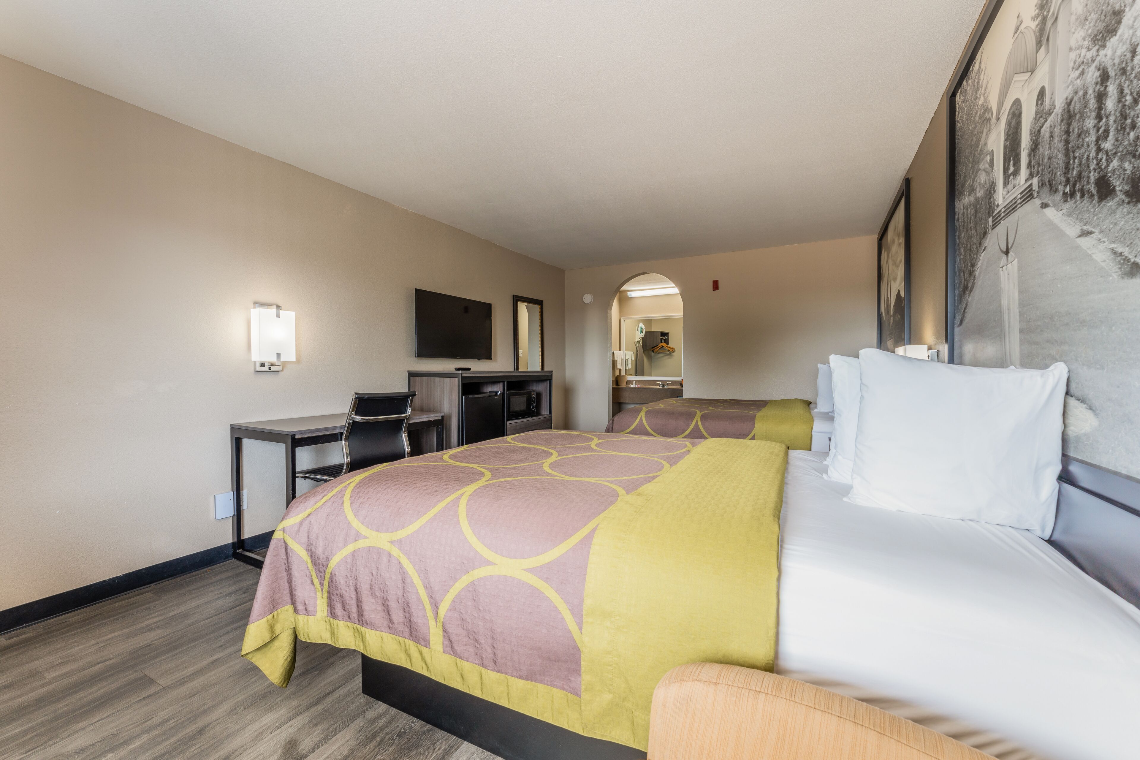 A hotel room with a large bed, a desk, a television, and a mirror.