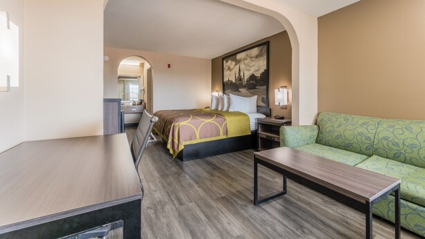 A hotel room with a bed, a green sofa, a wooden table, and a desk. - Super 8 by Wyndham Lake Charles Northeast (Lake Charles)