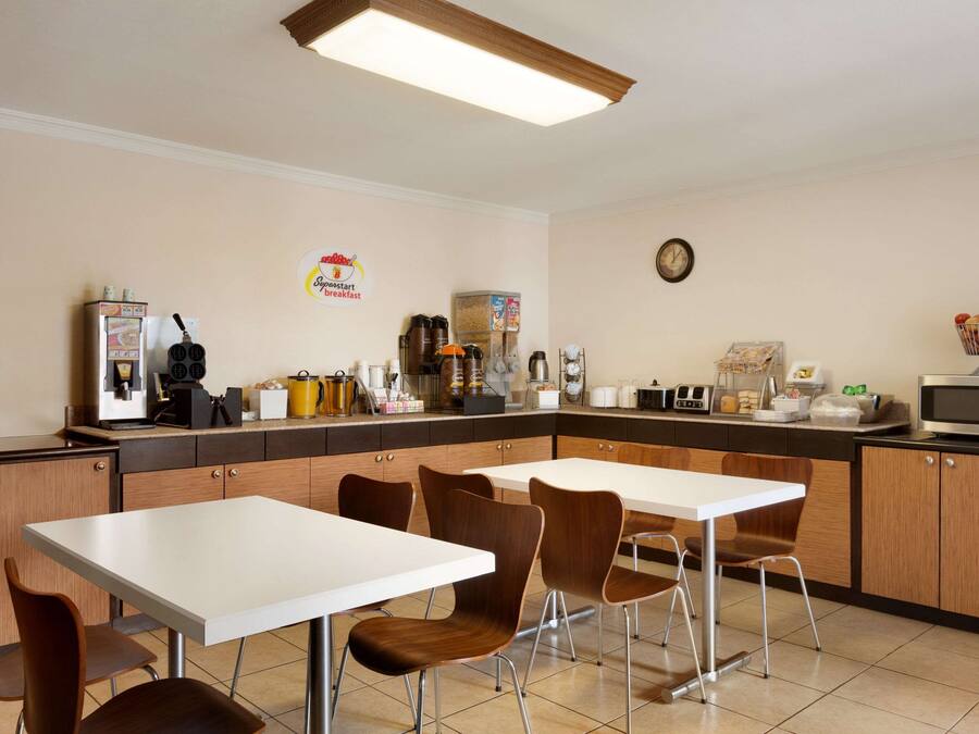 Une cuisine moderne avec des plans de travail blancs, des meubles en bois et un coin repas comprenant une table blanche et des chaises marron.
