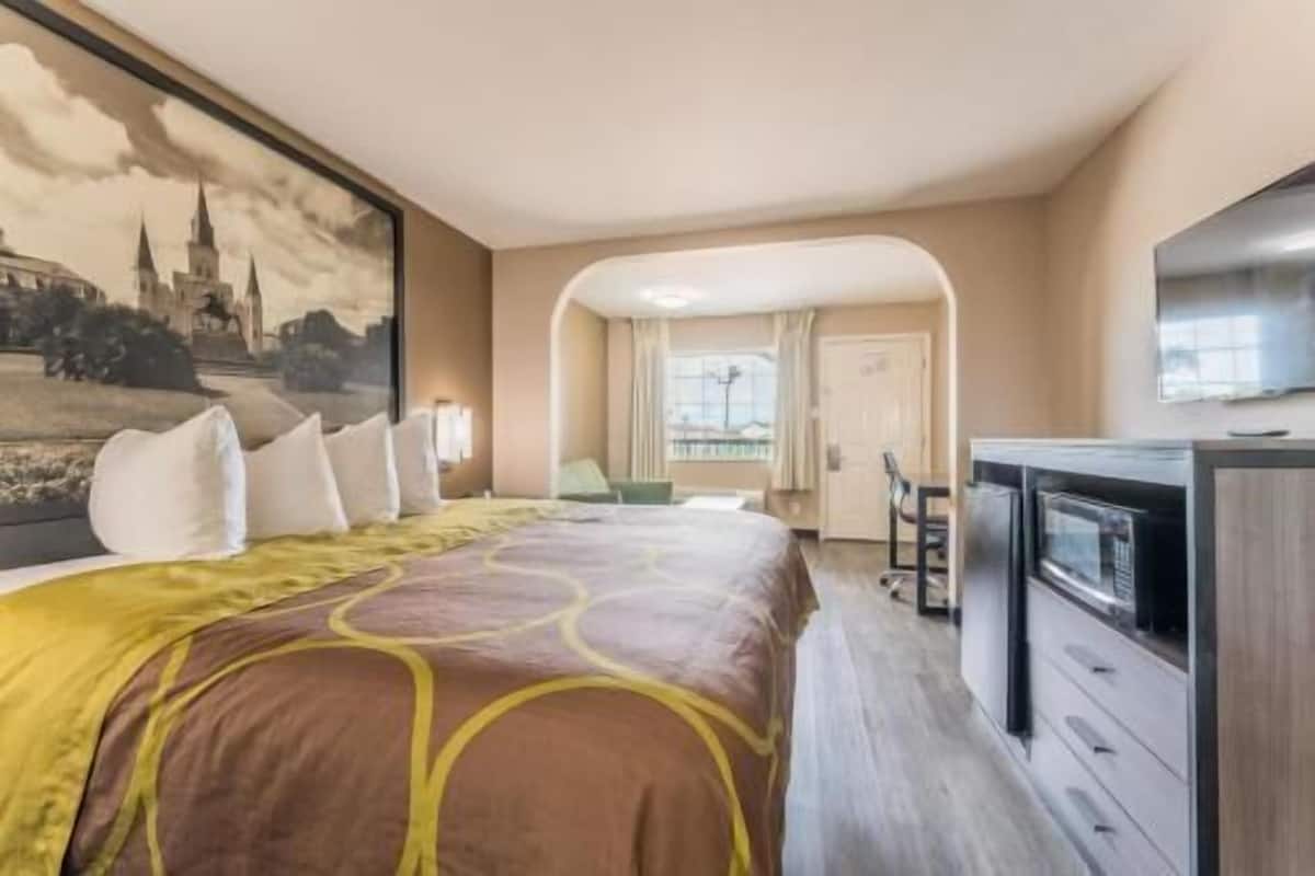 A hotel room with a bed, a desk, a TV, and a painting of a castle.