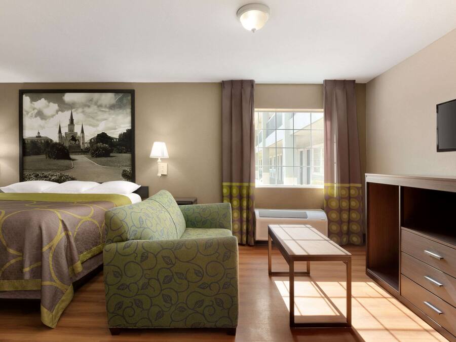A hotel room with a bed, a sofa, a TV, a desk, and a large window.