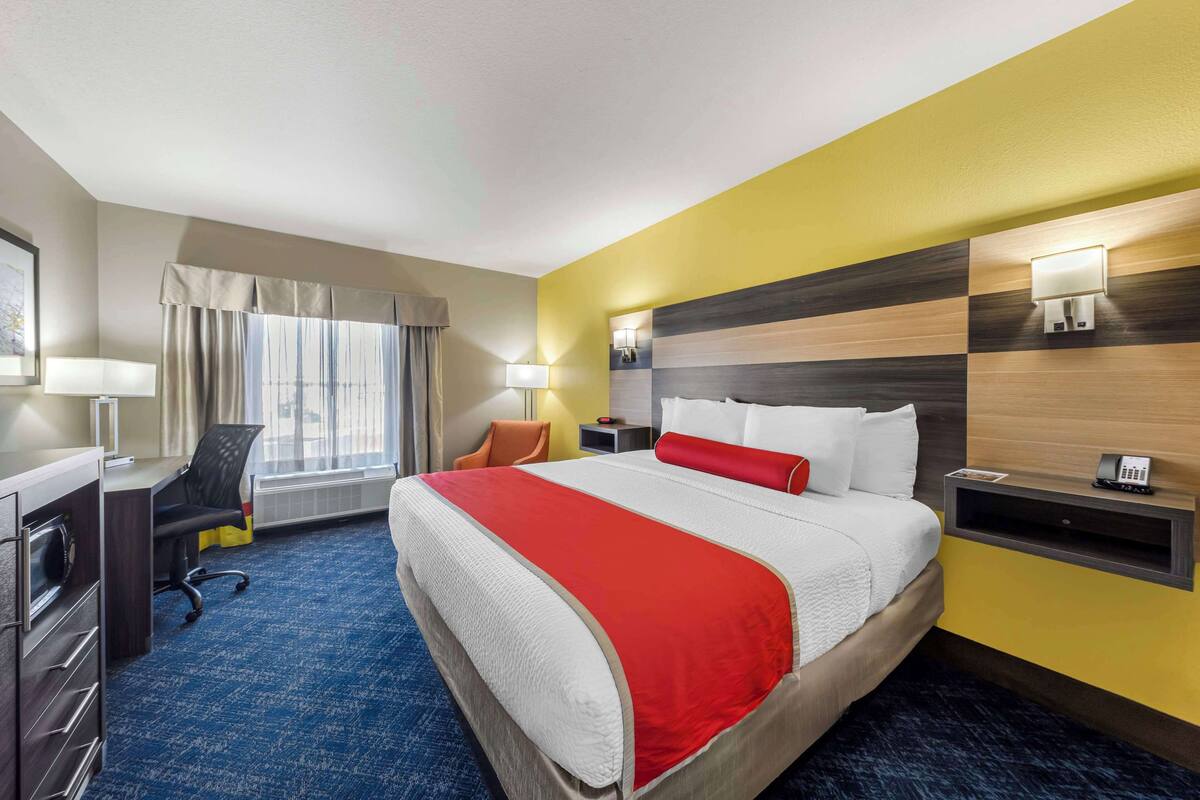 A hotel room with a large bed, a desk, a chair, and a window with curtains.