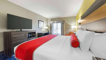 Ein Hotelzimmer mit einem großen Bett, einem Flachbildfernseher, einem Schreibtisch und einem Vorhangfenster.