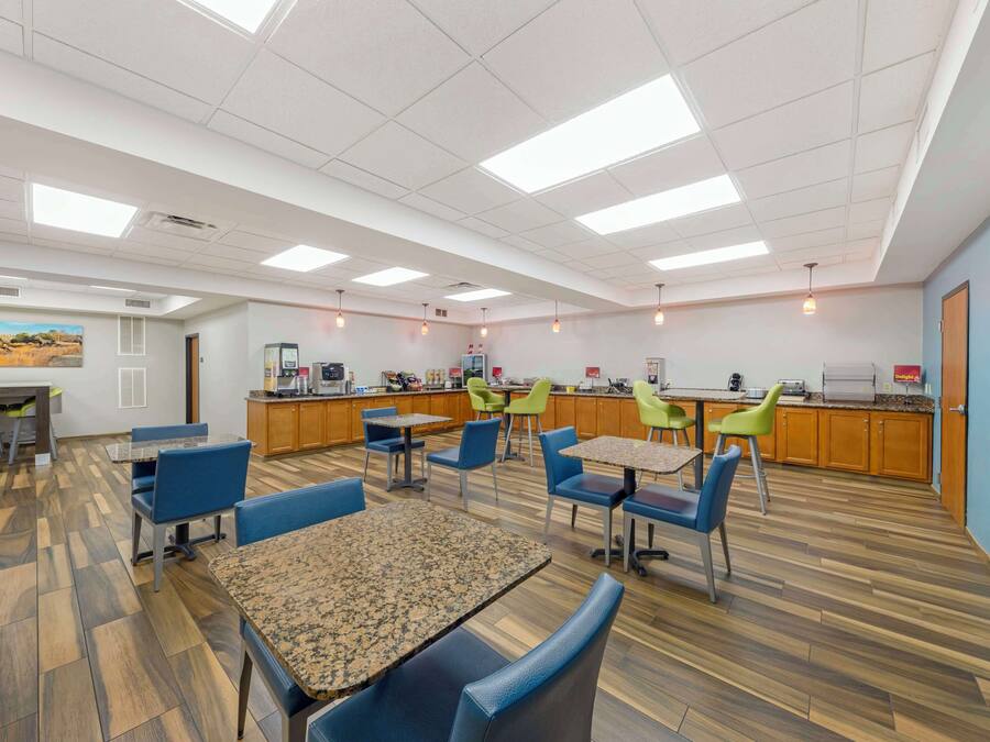 A dining area with multiple tables and chairs, a kitchen area with a counter and appliances, and a ceiling with fluorescent lights.