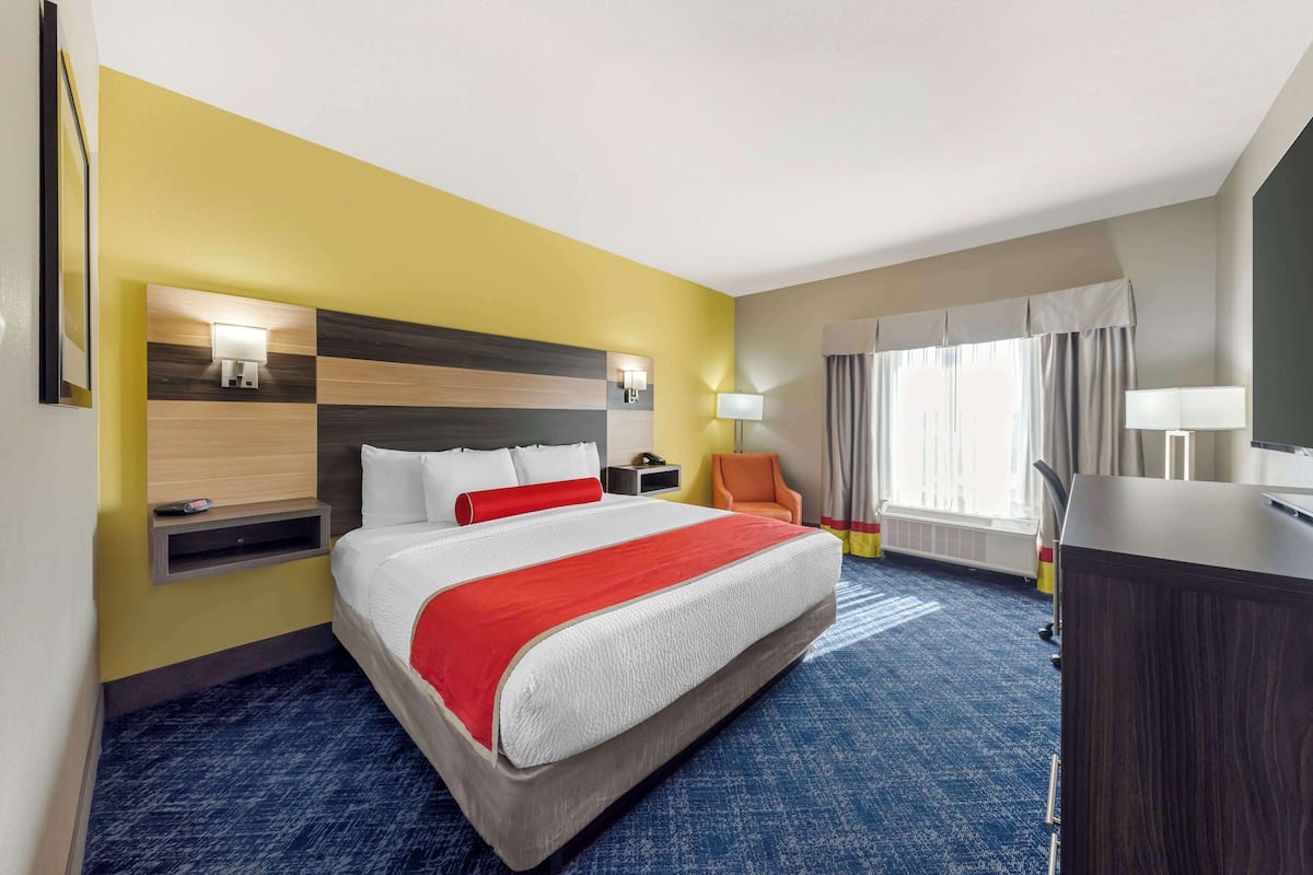 A hotel room with a large bed, a desk, a chair, and a window with curtains.