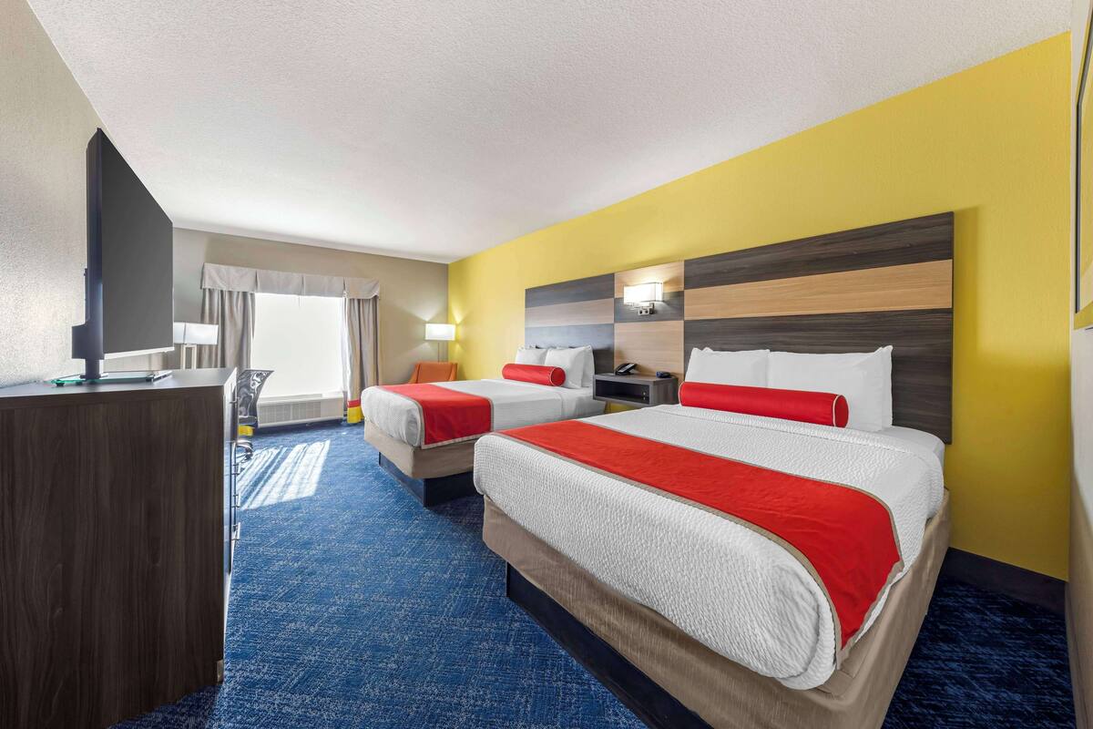 A hotel room with two beds, a desk, and a large window with curtains.