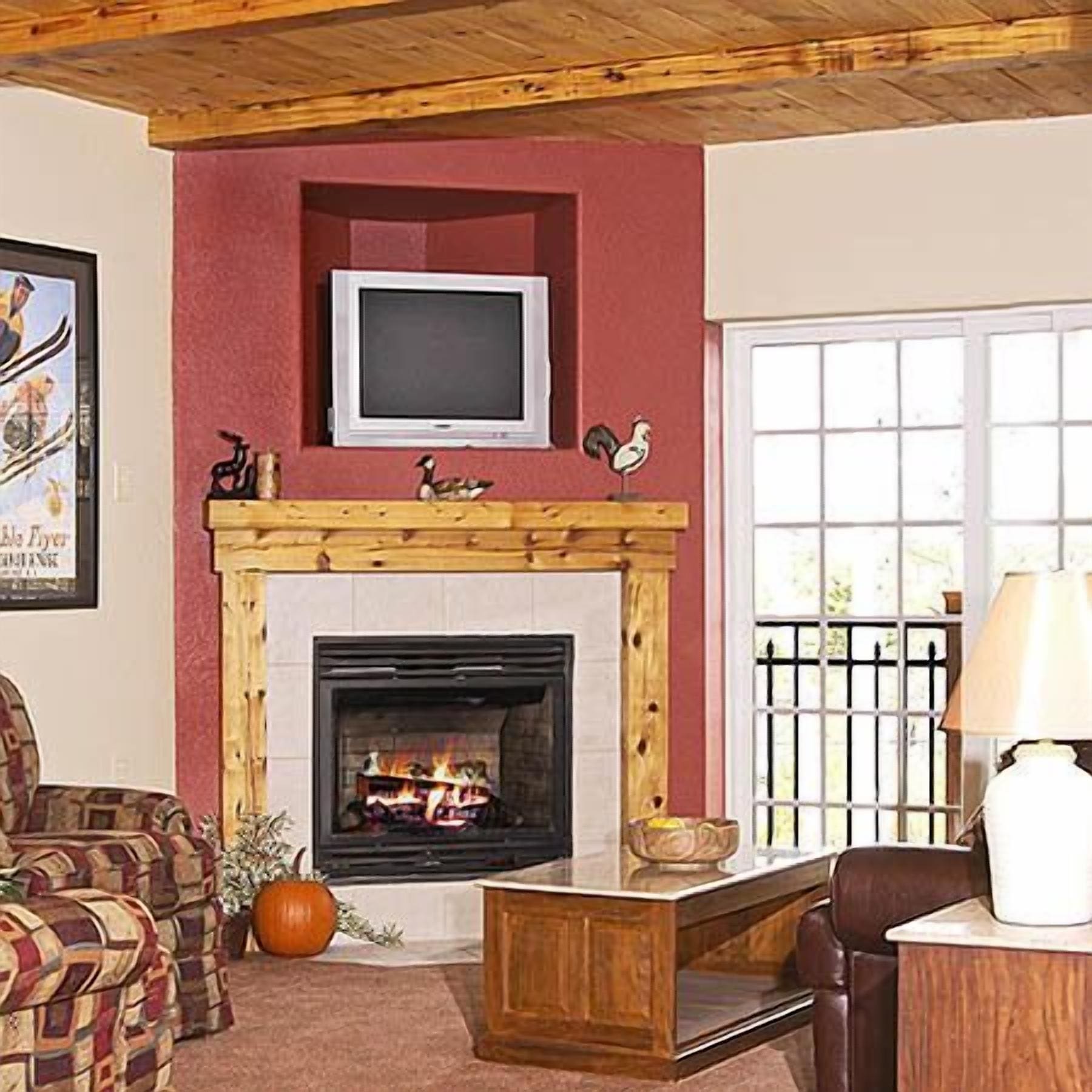 A living room with a fireplace, a television mounted above it, and a window with a view of the outdoors.