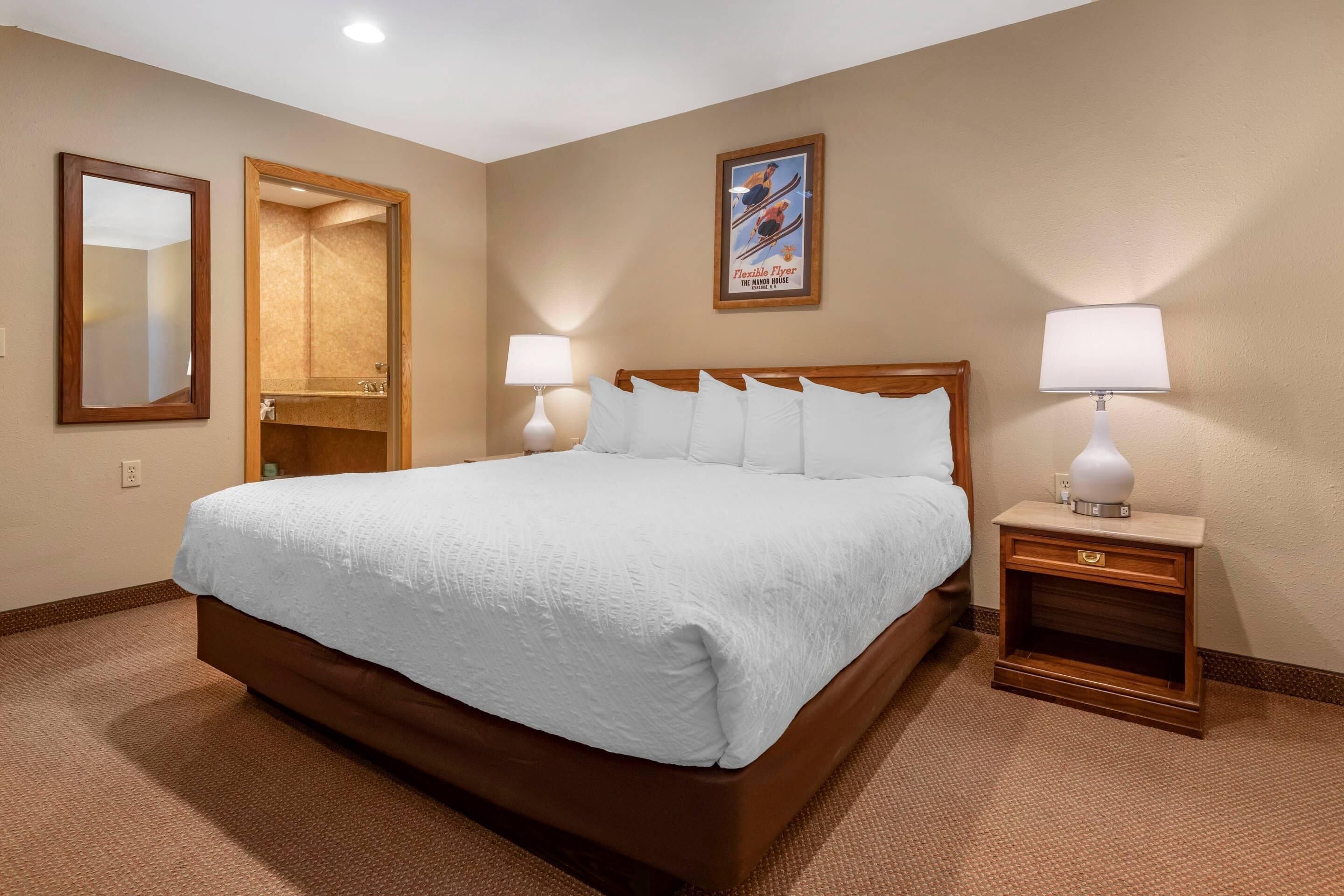 Habitación de hotel con una cama grande, dos mesitas de noche con lámparas, un espejo de cuerpo entero y un cartel en la pared.