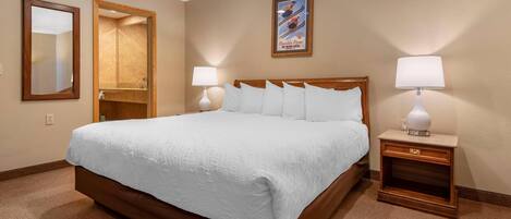 A hotel room with a large bed, two bedside tables with lamps, a full-length mirror, and a poster on the wall.