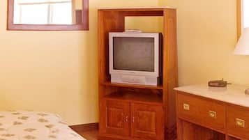 Una habitación de hotel con un mueble bajo de televisión de madera, una cama con colcha estampada y una mesita de noche con lámpara.
