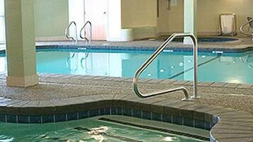 An indoor swimming pool with clear water, a tiled deck, and a metal ladder.