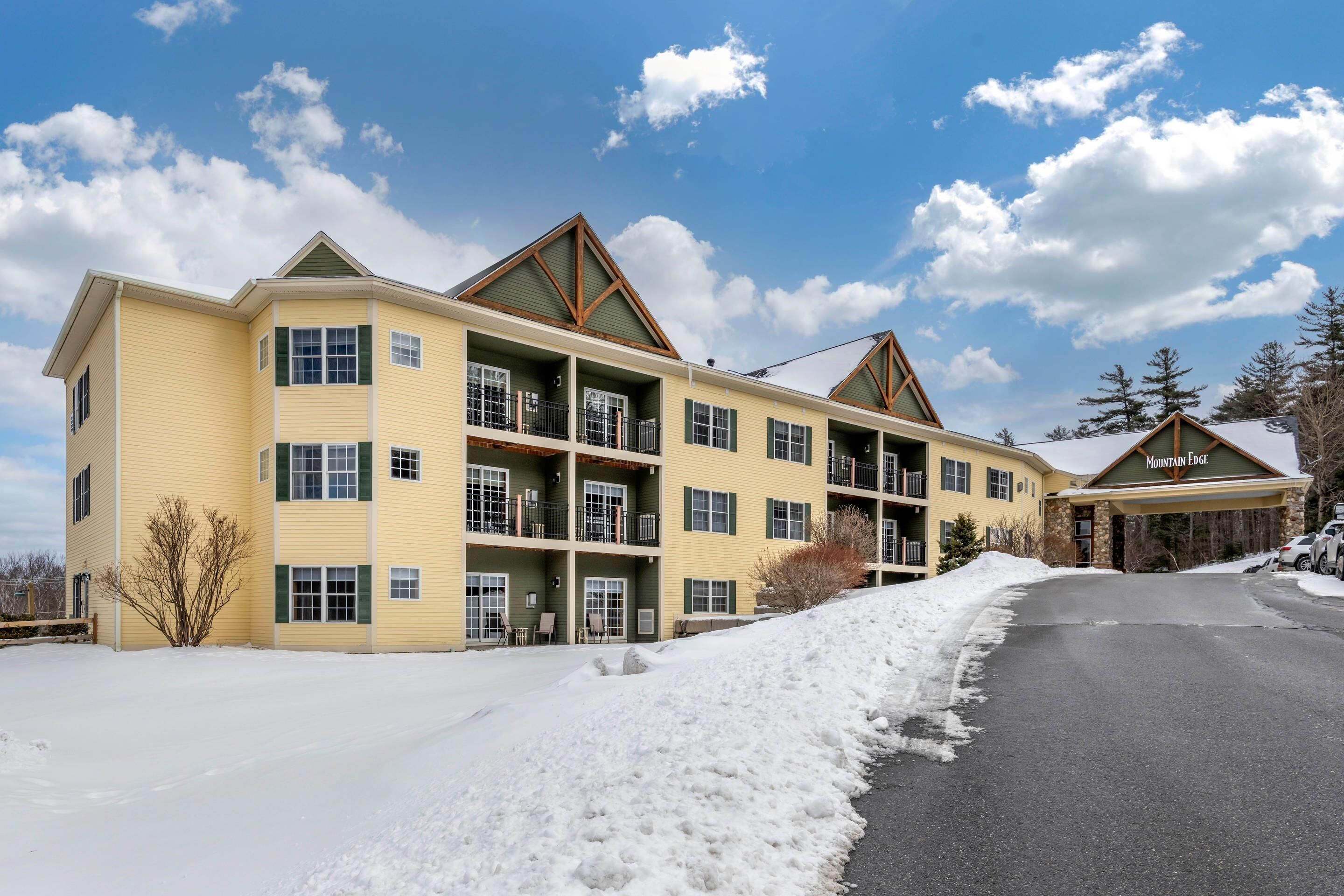 A multi-story hotel with a yellow facade, multiple balconies, and a snow-covered driveway.