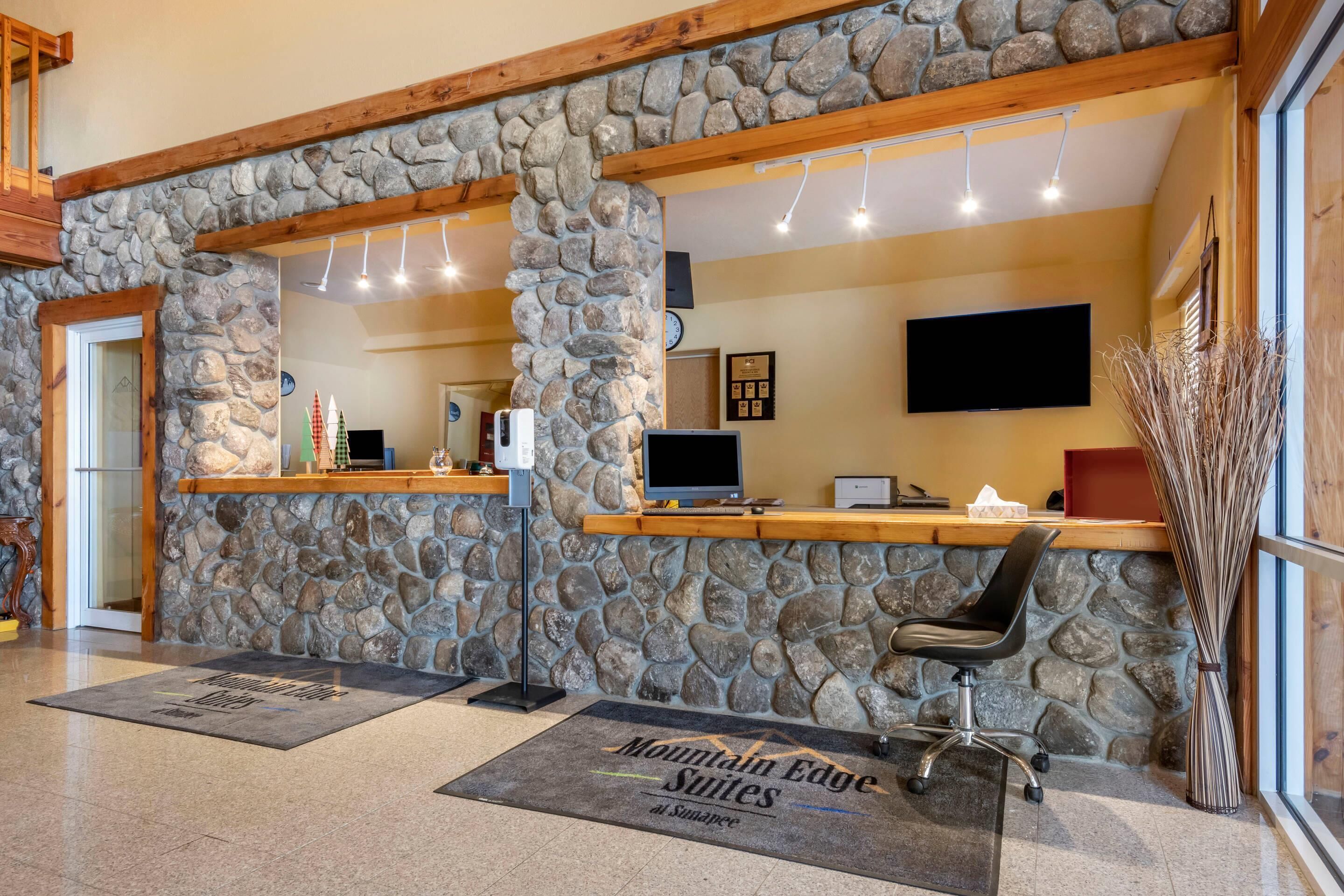 A reception area with stone walls, wooden beams, a reception desk, a computer, and a chair.