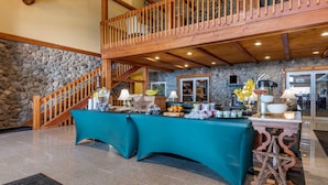 A spacious lobby with a high ceiling, a stone wall, a wooden staircase, and a buffet table.