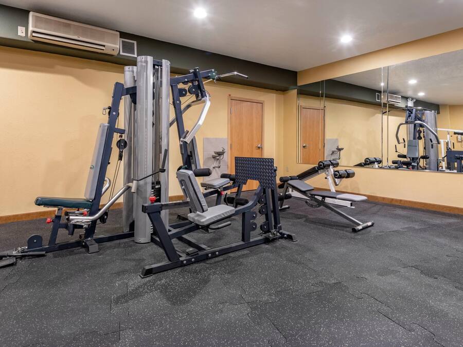 A gym with various exercise machines, a large mirror, and a door in the background.