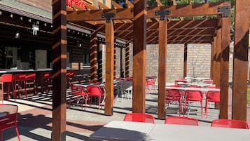 An outdoor patio area with wooden pergolas, red and white tables, and chairs.