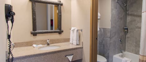 A bathroom with a granite countertop, a mirror, a hairdryer, a toilet, and a shower.