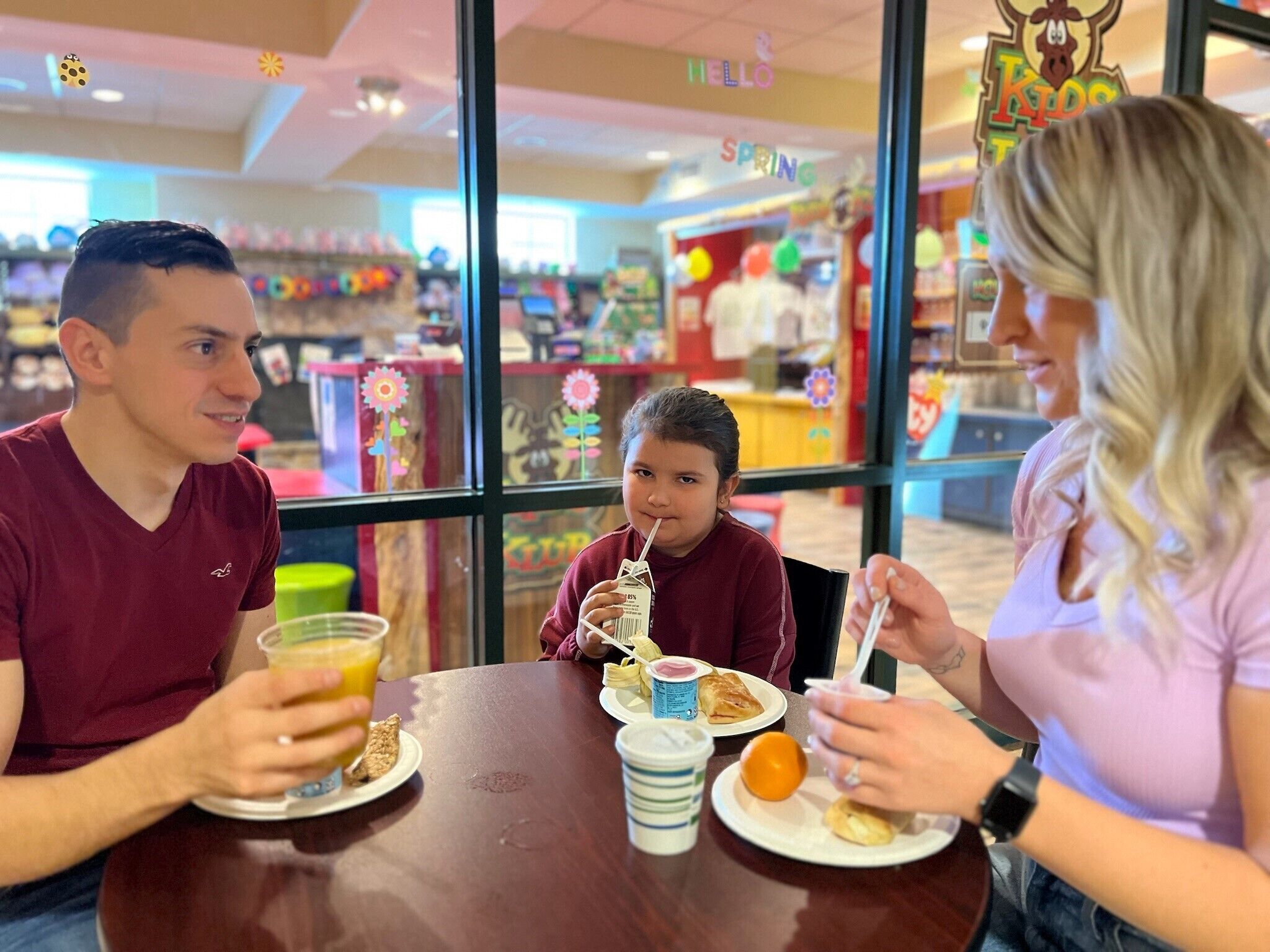 Une famille est assise à une table dans un restaurant, et on aperçoit en arrière-plan un espace de jeux pour enfants.