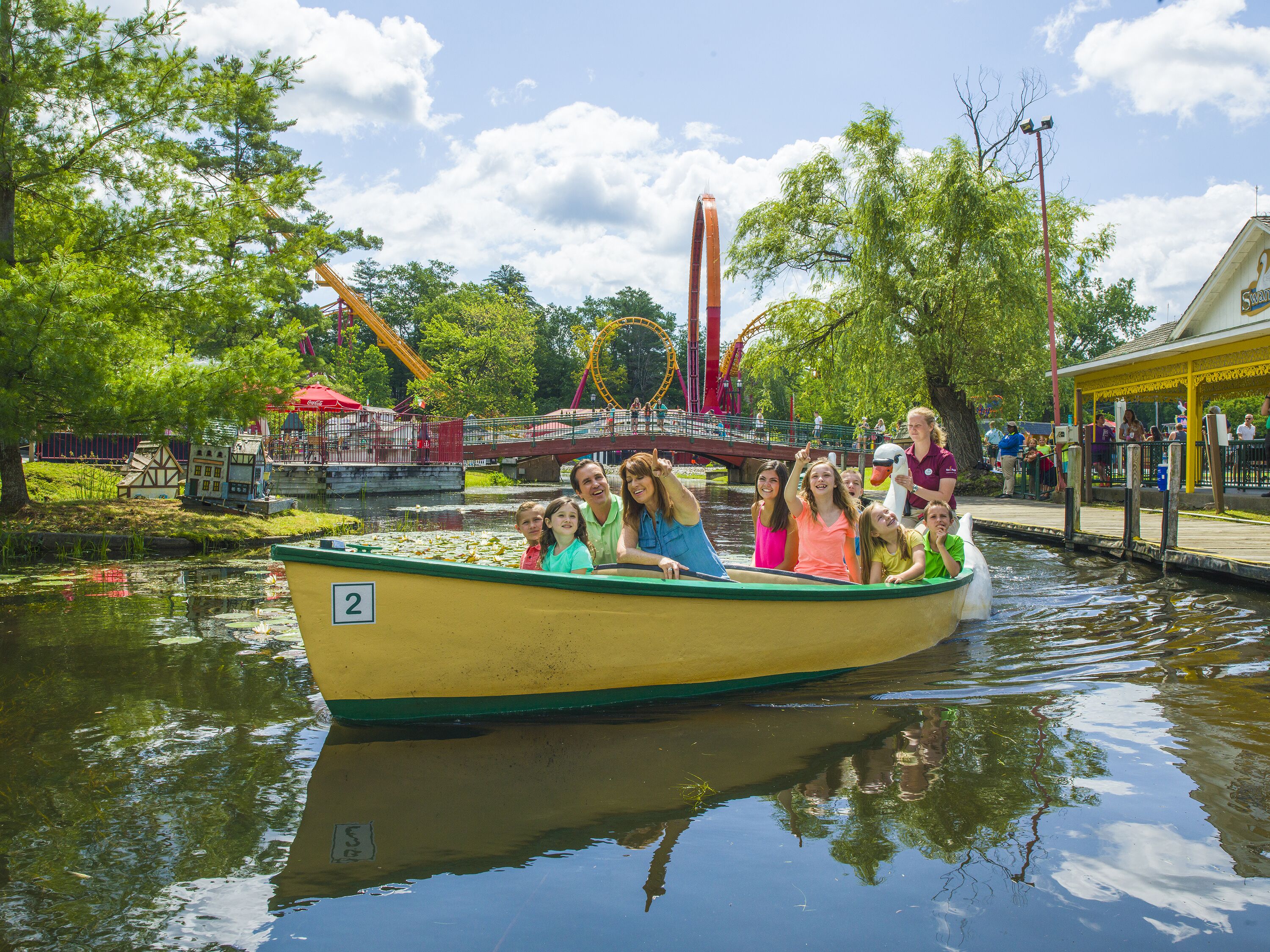 Un barco con gente, un puente y una montaña rusa al fondo.