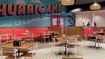 A restaurant interior with wooden tables and chairs, a large mural with the word "HURRICANE," and hanging wicker lamps.