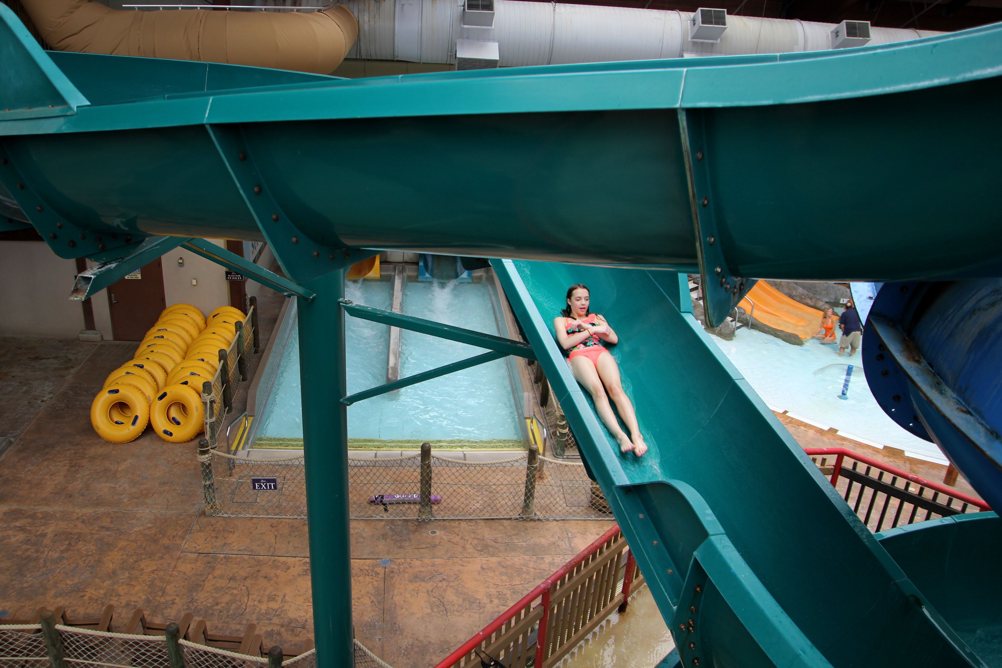Un toboggan aquatique avec une personne allongée dessus, une piscine et des toboggans aquatiques jaunes.