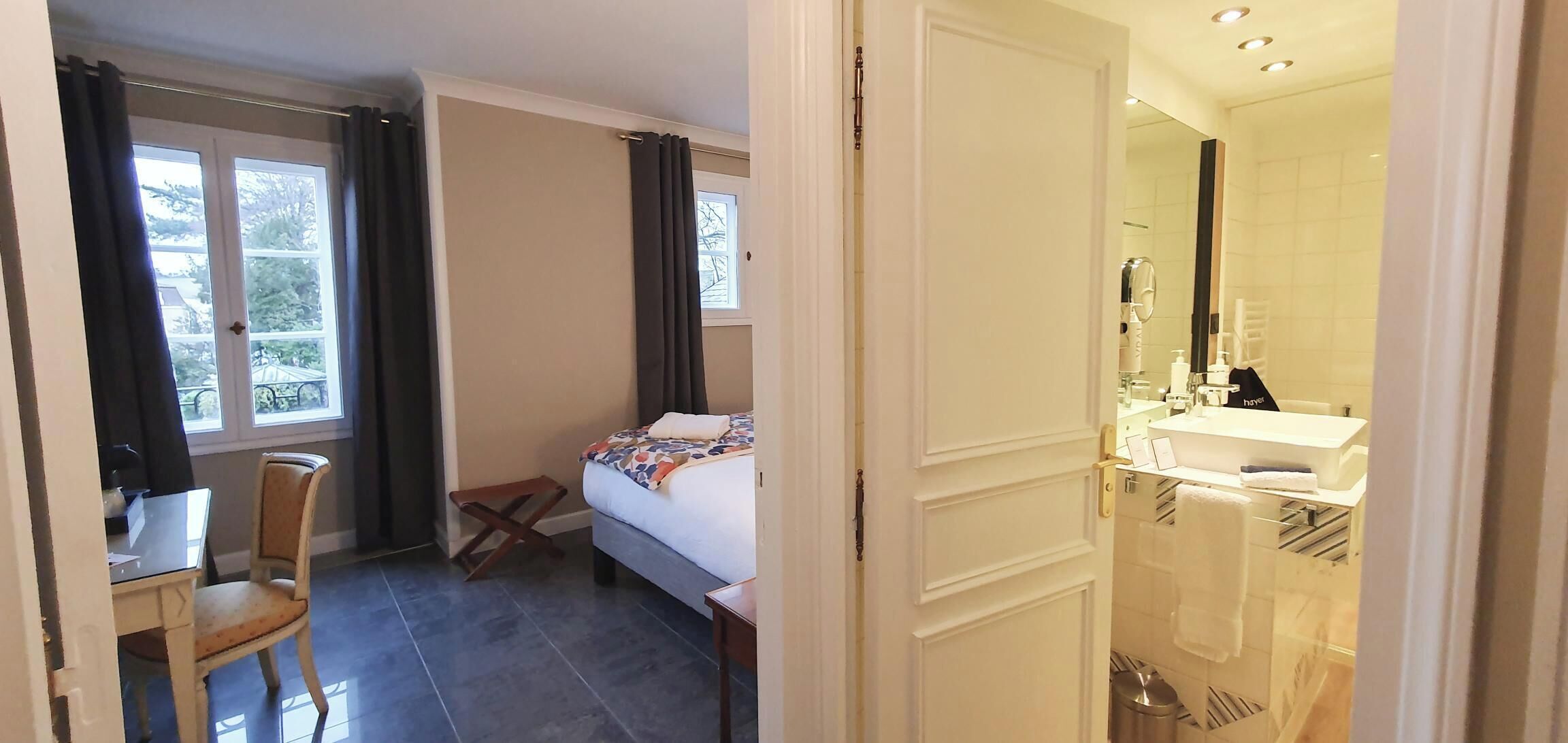 Un dormitorio con cama, una silla, una mesita y una ventana con cortinas.